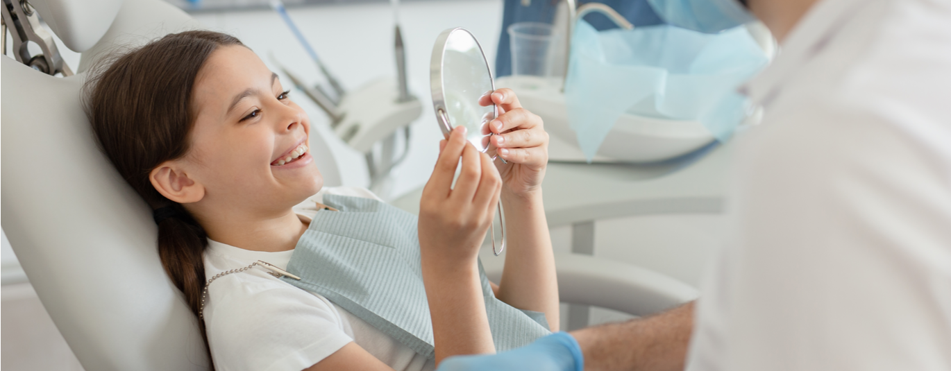Young girl at dentist's office smiles into handheld mirror